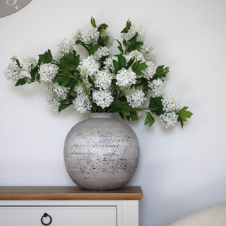 A round ceramic vase with a stone finish and a textured surface, primarily in grey colour with visible speckles with a hydrangea bouquet