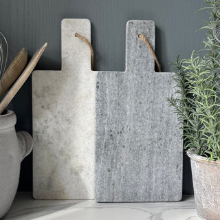 Set of marble cutting boards on a dark surface with a plant in the background
