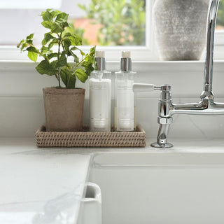 Two white bottles with silver caps on a kitchen counter next to a plant and faucet.