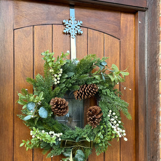 Green wreath with pinecones and white flowers on a wooden door