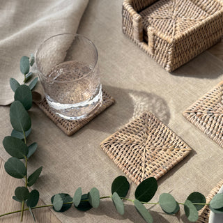 Glass of water on a woven coaster with eucalyptus leaves on a neutral-toned surface