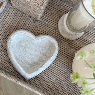 Heart-shaped stone dish on a textured surface with a glass vase and white flowers.