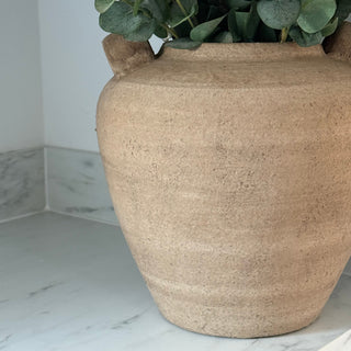 Beige ceramic pot with greenery on a marble surface
