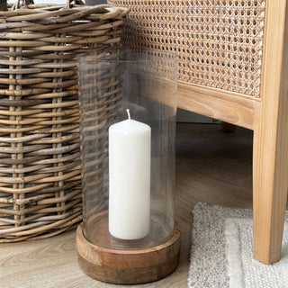 Clear cylindrical vase with a white candle inside on a wooden surface.