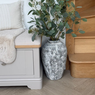 Decorative vase with greenery next to a light gray cabinet and wooden bench.