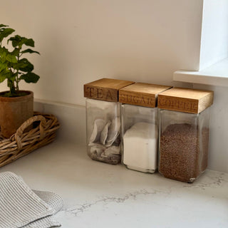Three glass jars labeled 'Tea', 'Sugar', and 'Coffee' on a marble countertop.