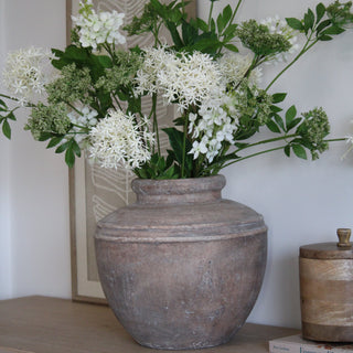 Decorative terracotta vase with white flowers and green leaves on a wooden surface.