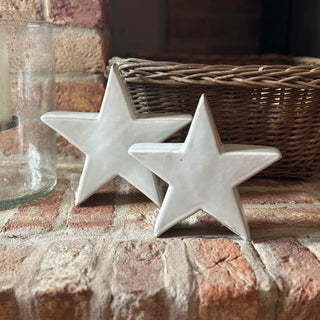 Two white ceramic stars on a brick surface with a wicker basket and glass container in the background.