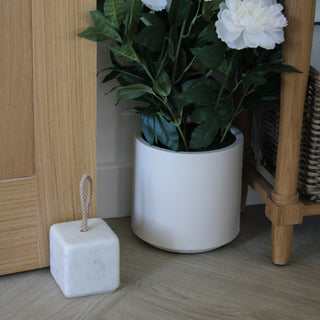 White potted plant on a wooden floor with a marble stop holding wooden door and basket in the background