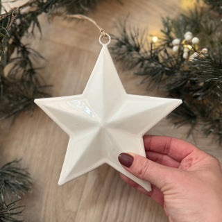White star ornament held by a hand with Christmas decorations in the background