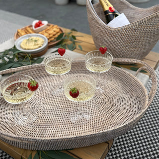 Wicker tray with glasses of champagne, strawberries, and a wine bottle on a checkered tablecloth.