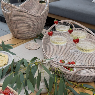 Outdoor setting with a woven table, food platter, and drinks on a patio.