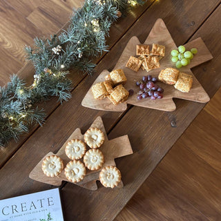 Wooden Christmas tree-shaped platter with snacks on a wooden table with a garland.
