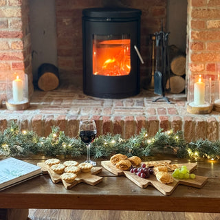Cozy fireplace scene with a table of food and wine, surrounded by festive decorations.